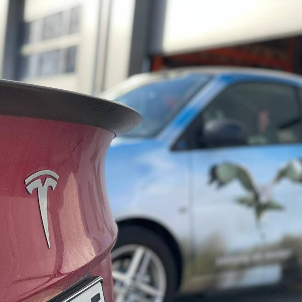 Ein rotes Auto auf der linken Seite und dahinter ist ein Smart mit einem Adler als Beklebung zu sehen