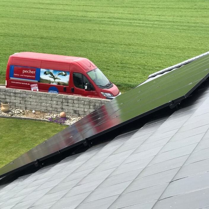 Ein rotes Auto einer Elektrofirma steht am Zaun. Auf dem Dach ist ein schwarze Photovoltaikanlage zu sehen