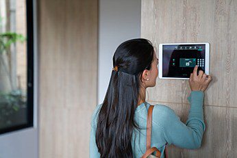 Frau bedient das Display einer Alarmanlage an der Wand